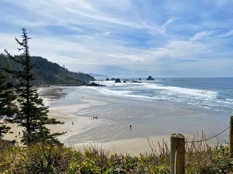 The view overlooking Ecola State Park - A sandy beach cove, ocean, and cloudy blue skies.