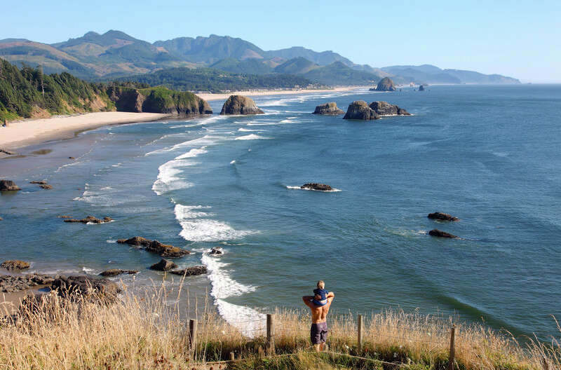 Father with baby on shoulders overlooking Ecola State Park in Oregon.