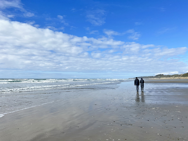 A couple looking for agates on an Oregon beach under blue skies with a few white clouds.