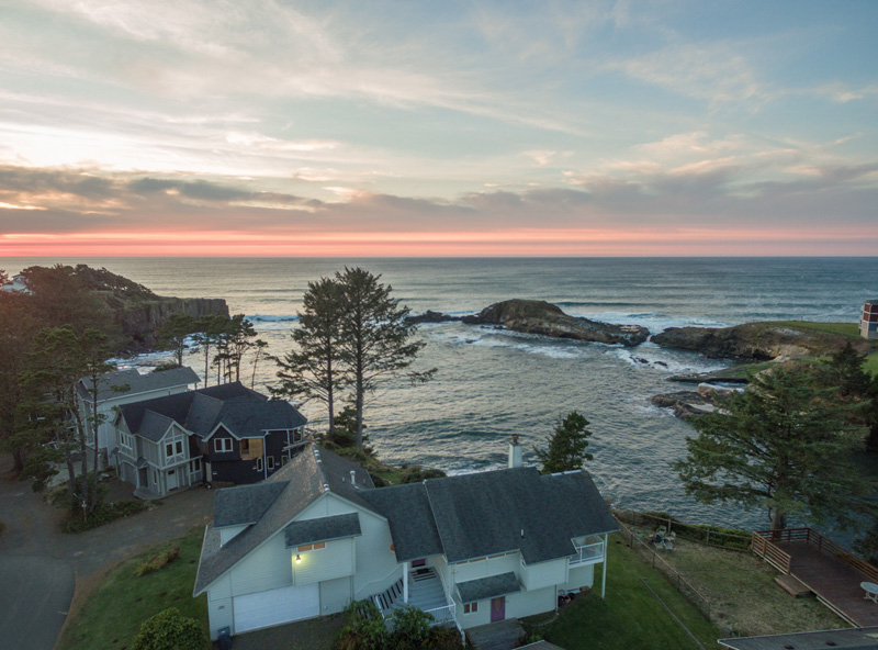 Aerial views at sunset of large oceanfront rental house in a rocky cove.