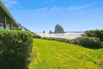 View from a beach house deck of people on a sandy beach, the Pacific Ocean, and Haystack Rock on a sunny day.