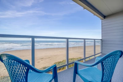 2nd-story balcony of 2 blue chairs overlooking the ocean on a clear sky day.