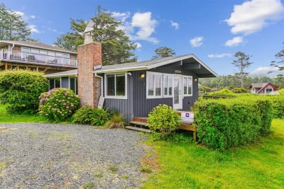 One level, dark gray little cottage with white trim and wrap around deck.
