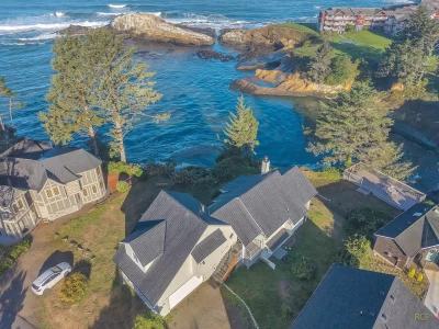 Aerial view of 2 story large oceanfront house on a rocky cliff.