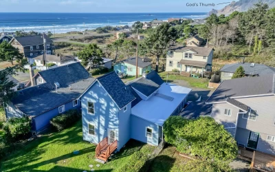 Aerial view of blue beach house with a green grass yard in a neighborhood with the ocean in view.
