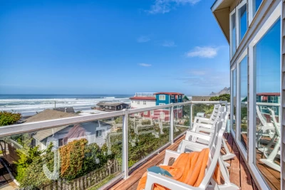 Four white chairs on a beach house deck high on a hill overlooking houses and a beautiful ocean view on a blue sky day.