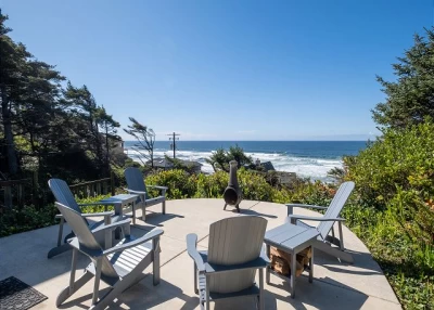 Five blue/gray Adirondack chairs sitting on a round patio with an ocean view and a chiminea.
