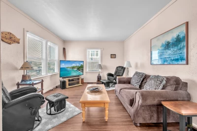 Living room in older home with updated tans and turquoise decor, a brown sofa, large TV, and 2 rocker lounge chairs.