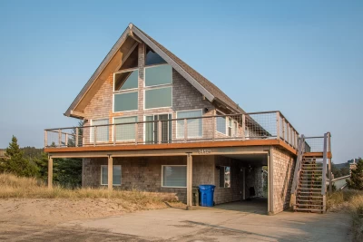 Beach house open dining/living room with a wall of windows and open beam cedar ceiling. Views of neighboring houses, Haystack Rock and Cape Kiwanda.