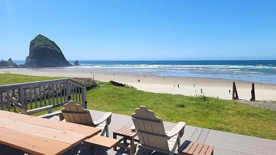 Oceanfront deck with Adirondack chairs, grassy yard, beach stairs, and a close view of Haystack Rock!