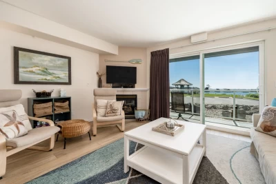 Bay views from living room with tan, cream, and soft turquoise colors. A gas fireplace and TV.