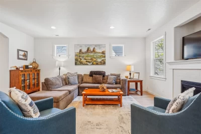 Formal living room with white walls, brown sectional, 2 blue chairs, gas fireplace with a TV over the top.