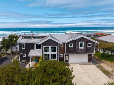 Aerial view of 2-level gray cedar shingled beach house with ocean views.