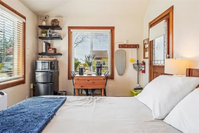 A studio room with a bed, white linens, 2-chair table, small fridge, and microwave.
