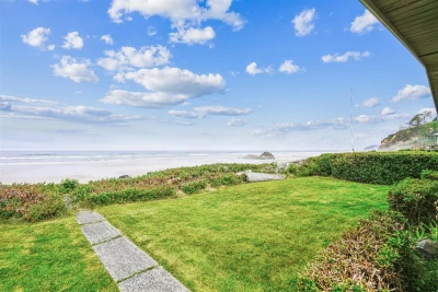 A green grassy yard, and a cement pathway leading to a sandy beach.