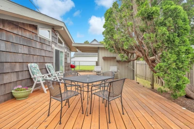 A fenced-in back deck of a beach house with outdoor furniture and BBQ.