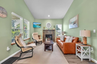 Living room with sea green walls, a gas burning fireplace, leather sofa, 2 chairs, and a TV mounted on a corner wall.