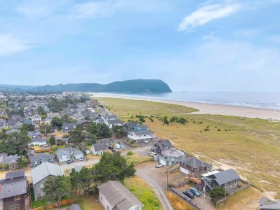 Aerial view of houses along a grassy beachside shoreline with a sandy beach, a mountainside, and blue ocean. ocean.