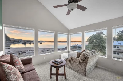 A living room surrounded by windows with a bay front view and a sandy beach during a beautiful sunset.