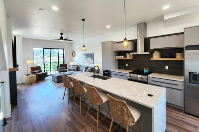 Cozy living room with sofa, rectangular fireplace, kitchen island, and large sliding glass door to the deck
