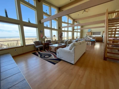 Aerial view of 2 story house, prow front is all oceanfront windows and deck. Ground level deck with hot tub and glass railing.